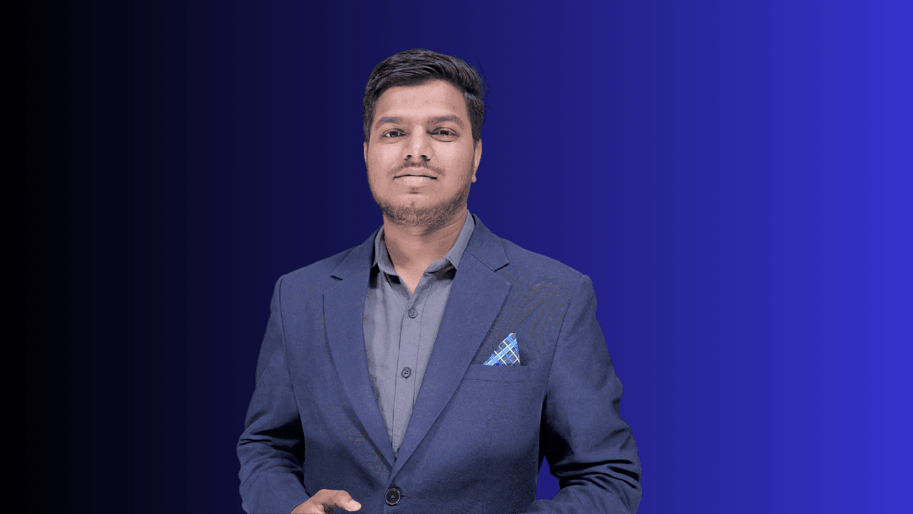 Man in a blue blazer with a pocket square and gray shirt, standing against a gradient background.