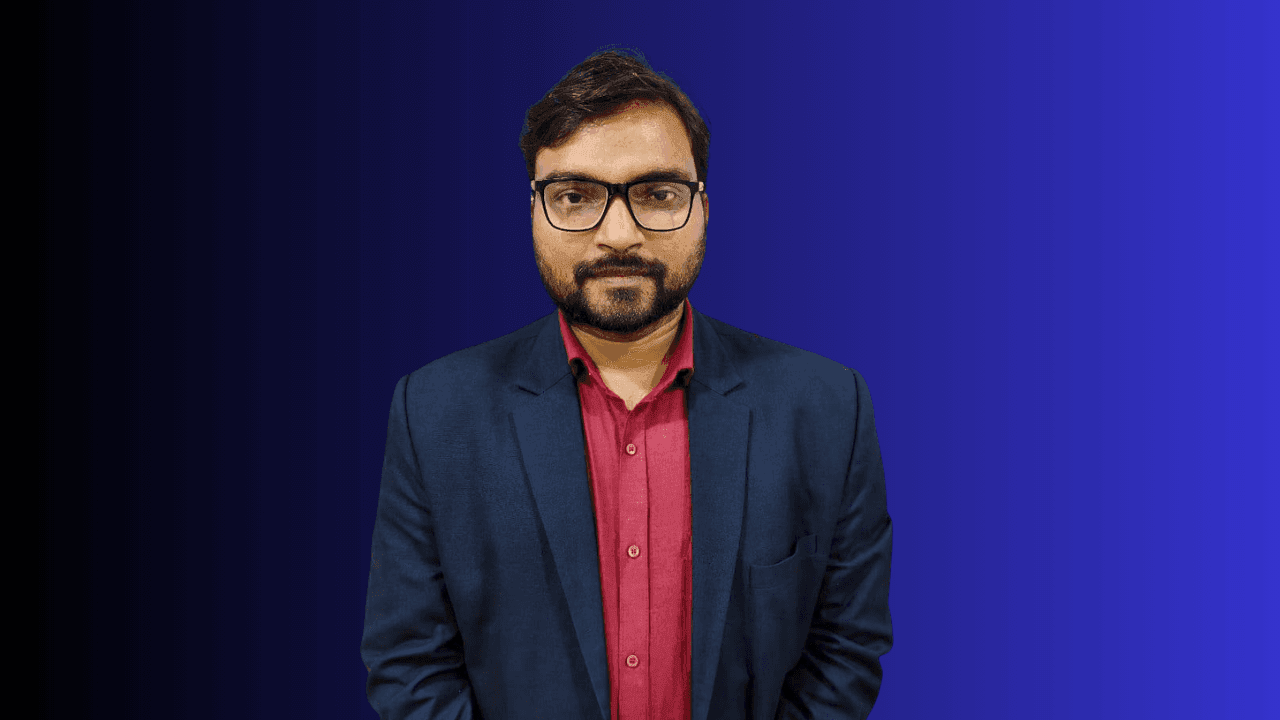 Person wearing a dark blue blazer over a red shirt, standing against a gradient blue background.