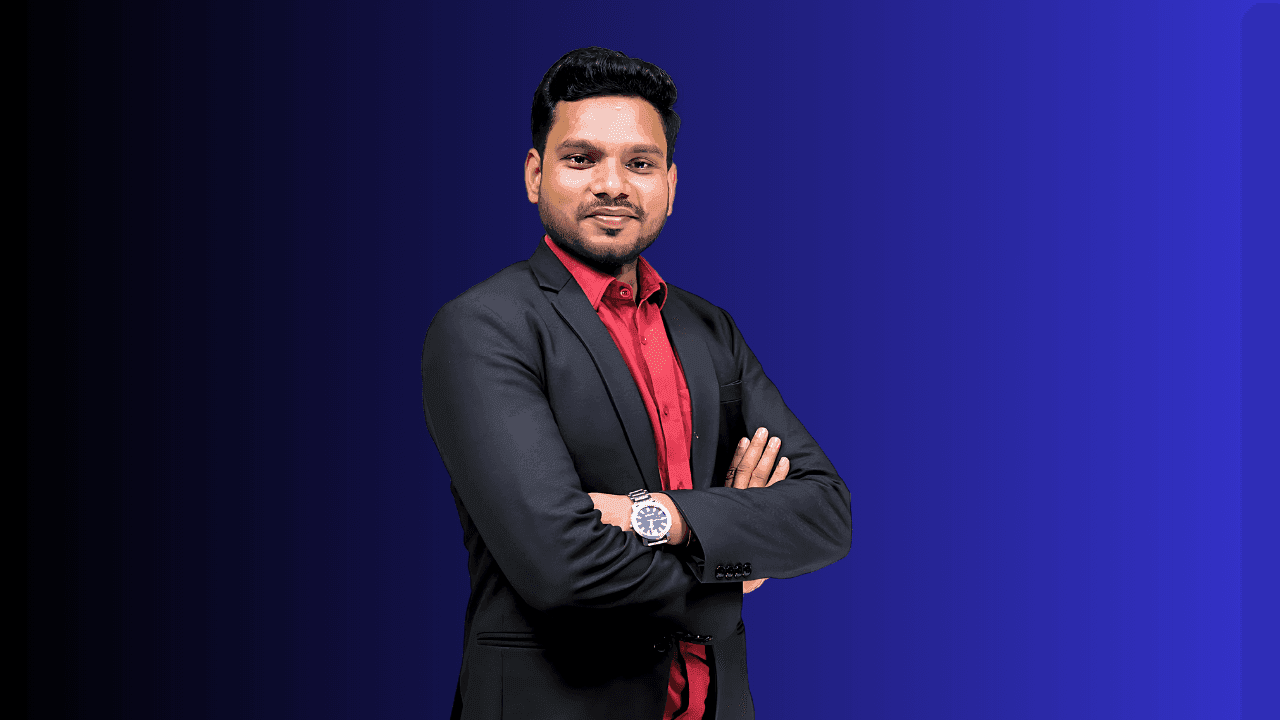 Man in a red shirt and black blazer with arms crossed on a blue gradient background.